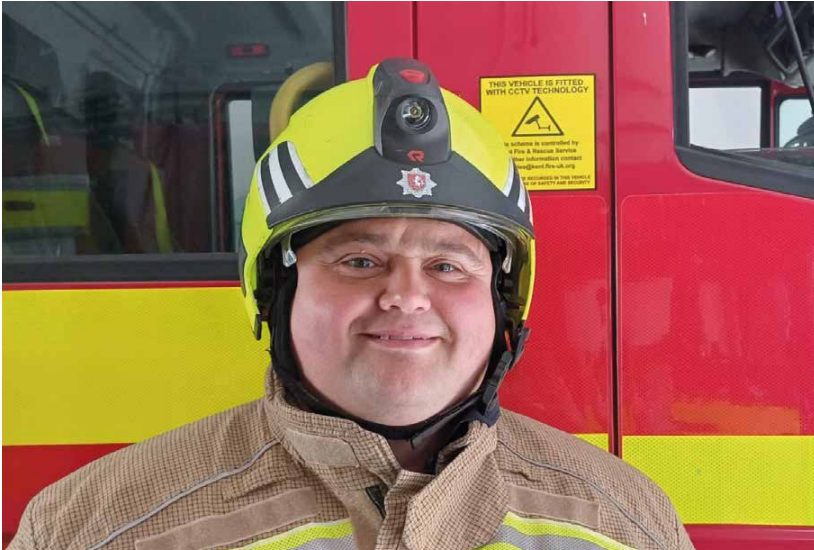 Dave Turner smiles at camera wearing firefighter helmet 