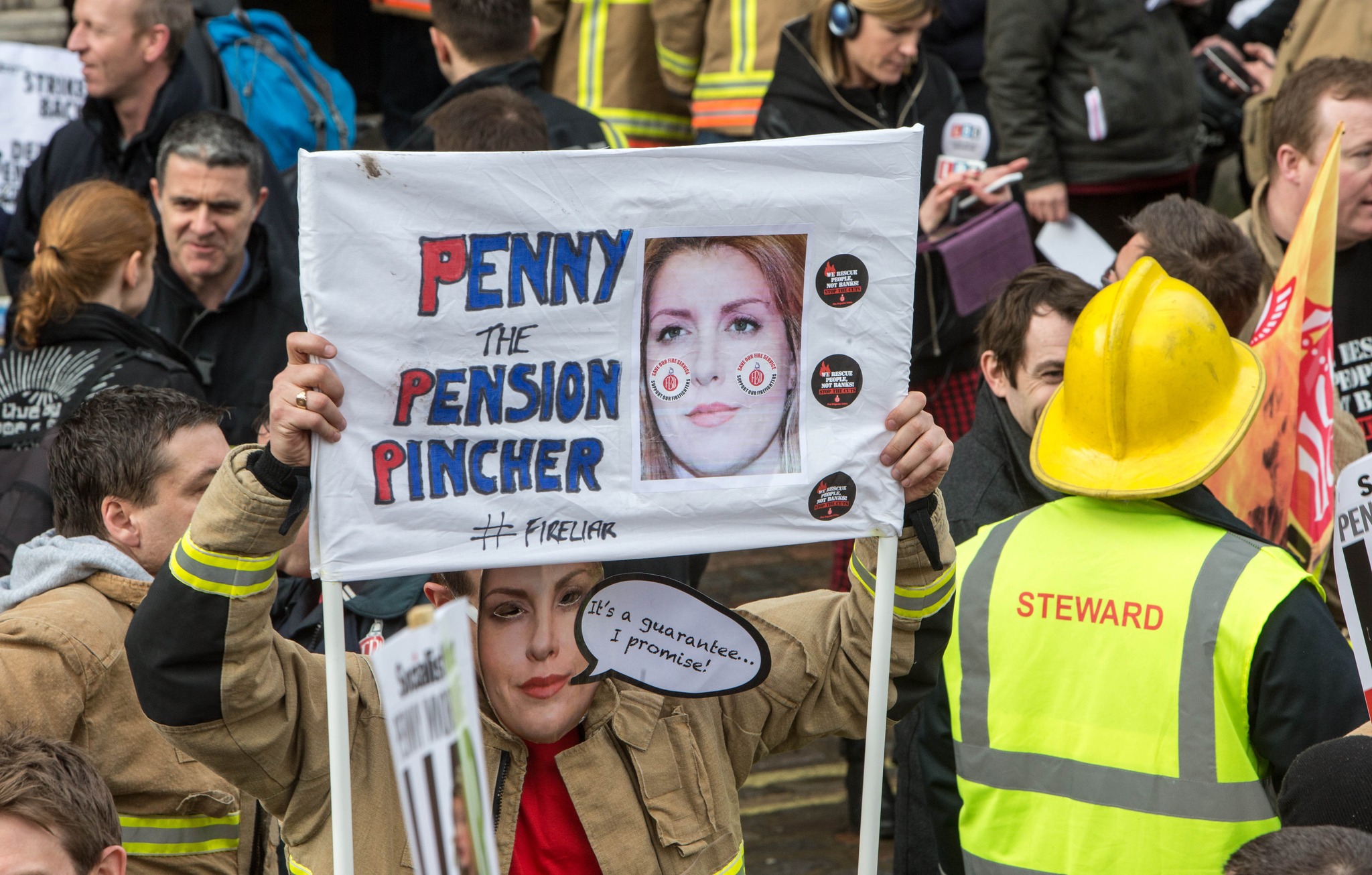 Firefighter holding sign that reads 'Penny Mordaunt penny pincher'