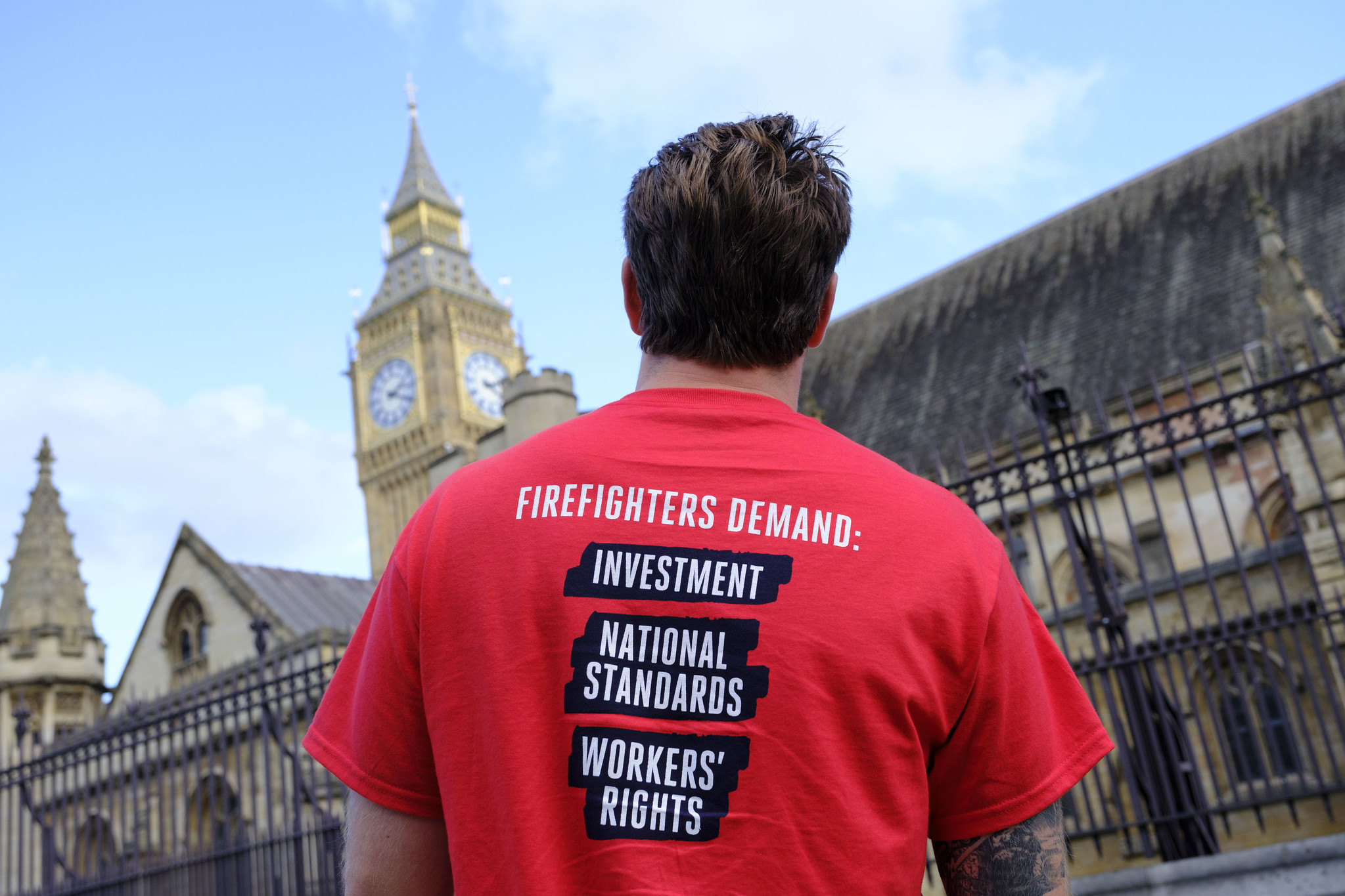Firefighter outside parliament wearing t shirt reading 'Firefighters demand investment, national standards, workers rights'