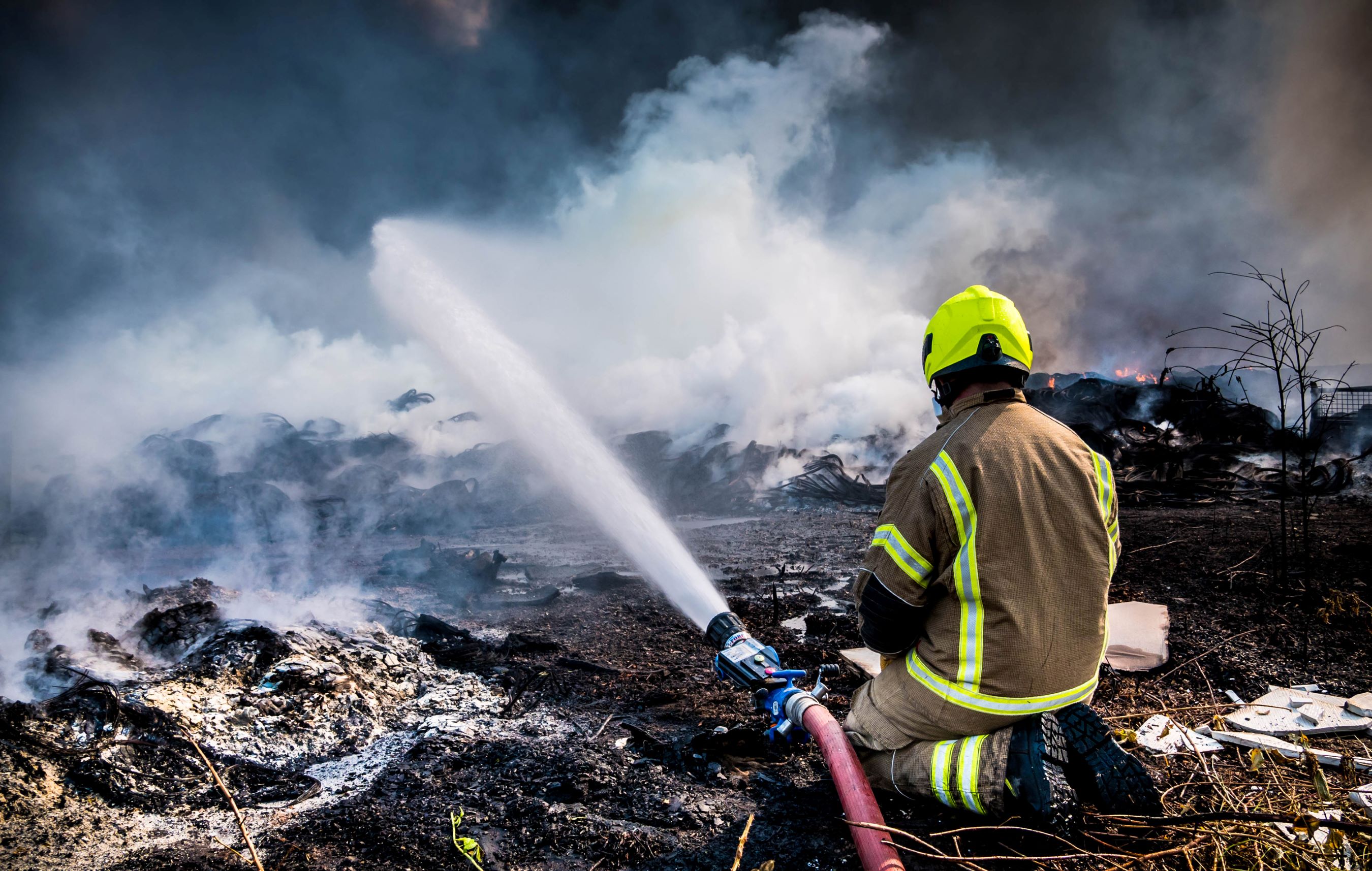 Firefighter sits next to hose while responding to a large fire outdoors