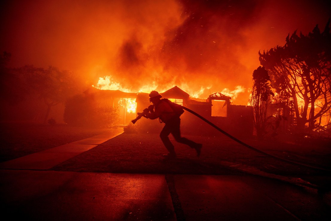 Firefighter drags a hose in front of burning buildings in LA
