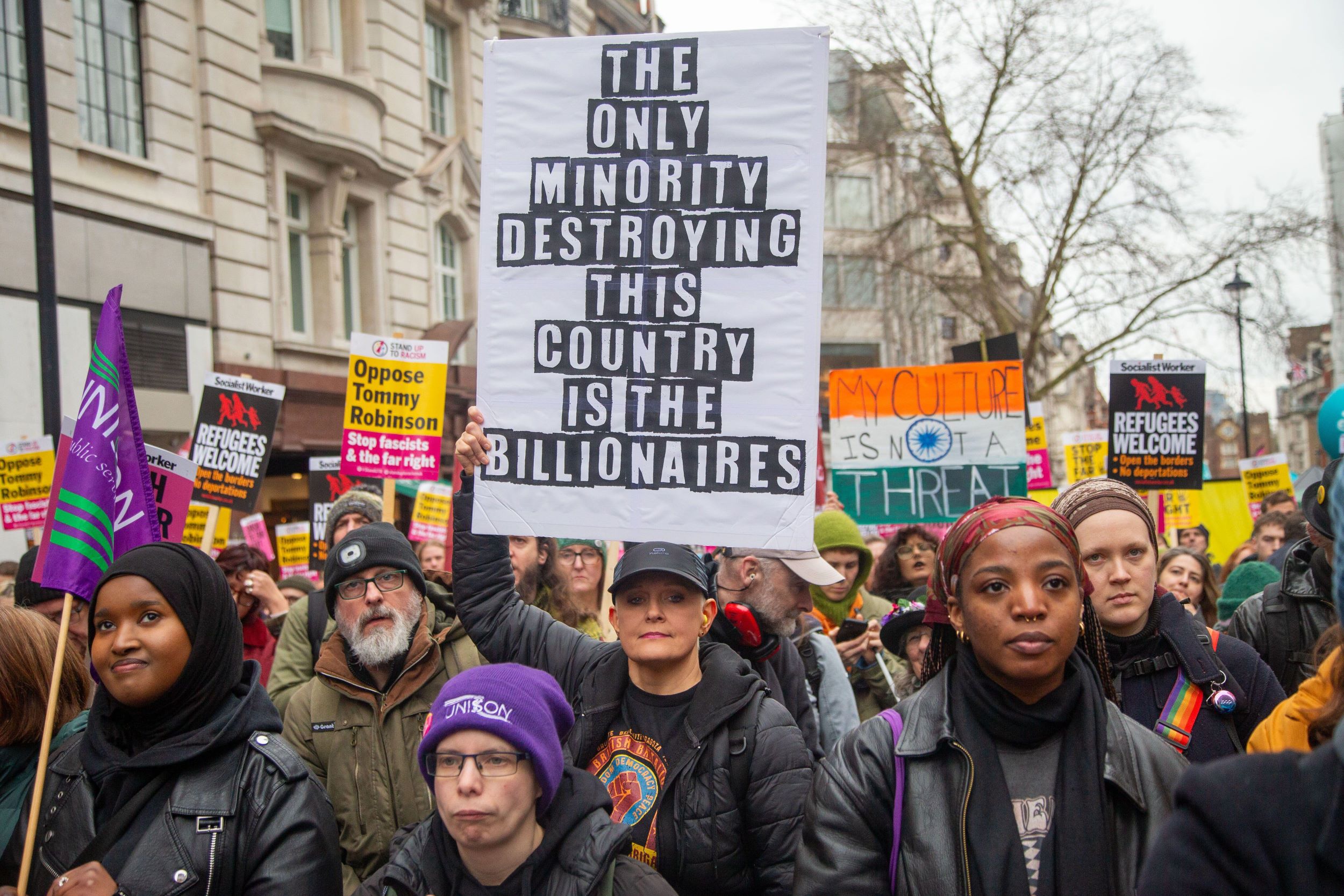 People at a protest against racism holding a placard reading 'the only minority destroying this country are the billionaires'