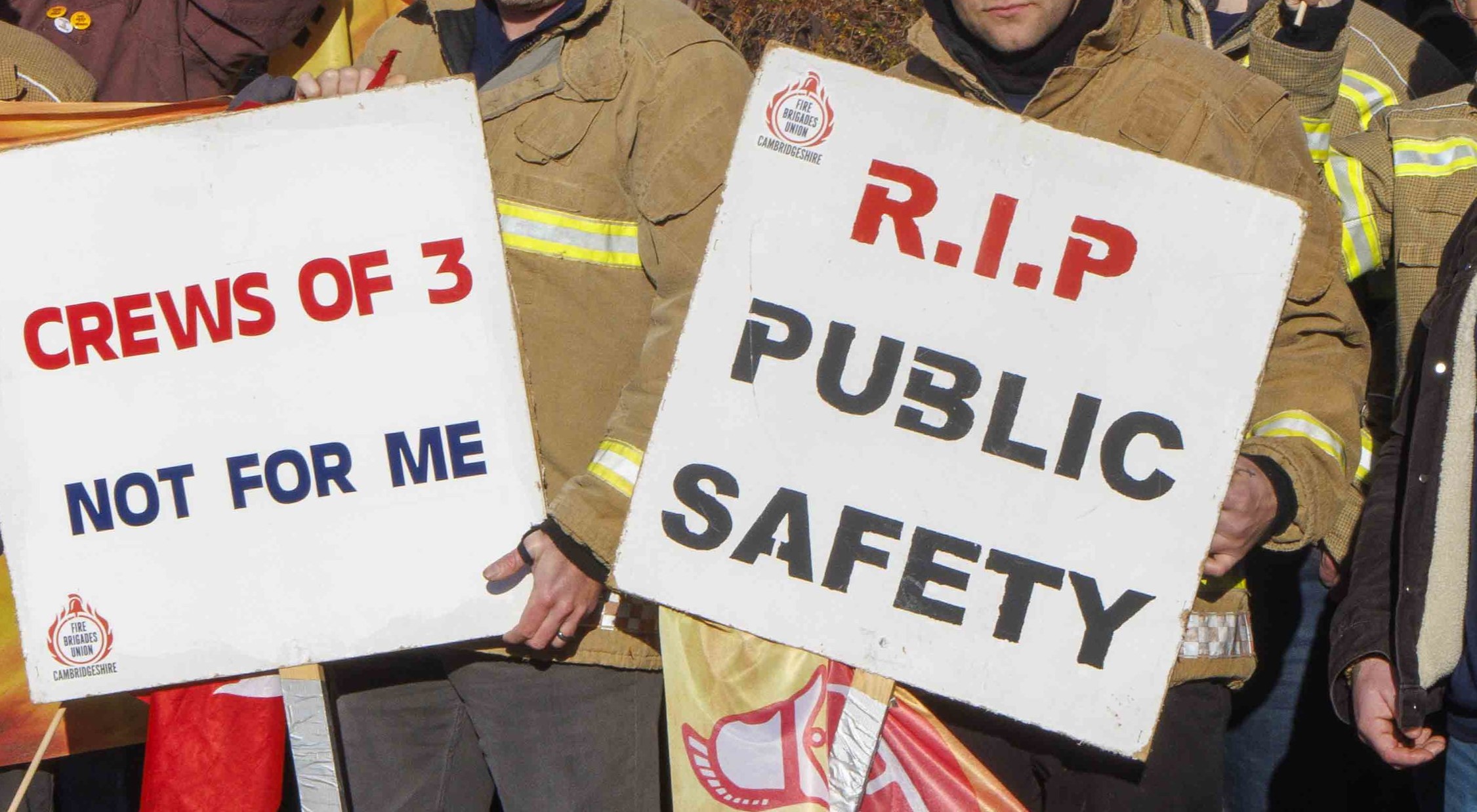 Two firefighters hold signs reading 'crews of three, not for me' and 'RIP public safety'