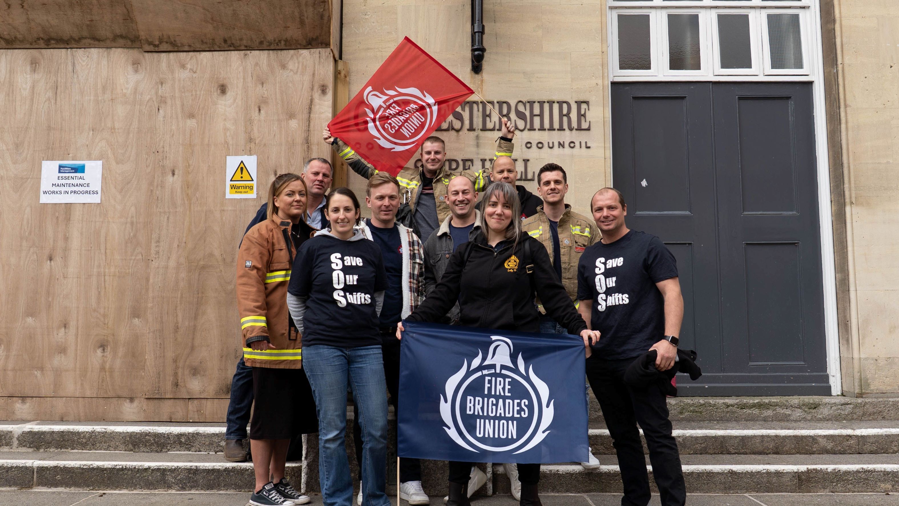 A group of FBU members hold flags outside Gloucestershire county council building