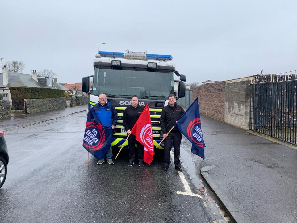 Three FBU members with flags stand in front of the donated fire engine