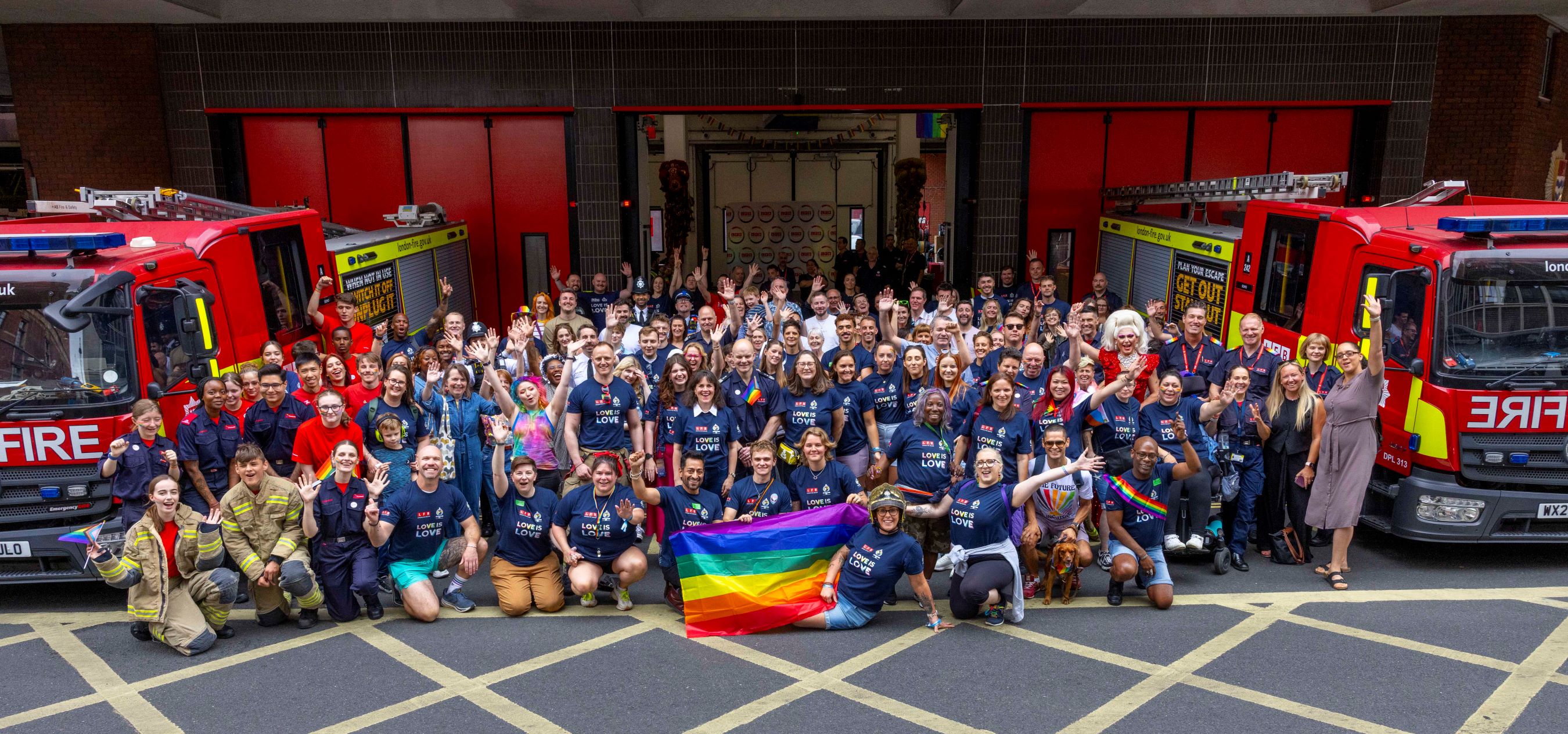 A large group photo with rainbow pride flags outside a fire station