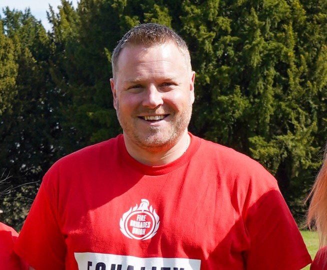 Ben Selby smiles at camera wearing a red "Equality matters" t shirt