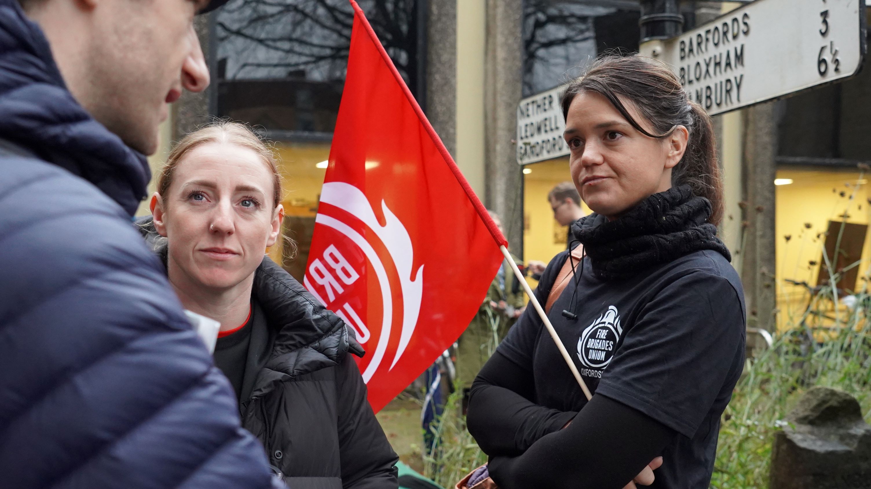 A woman holding an FBU flag while talking to fellow union members