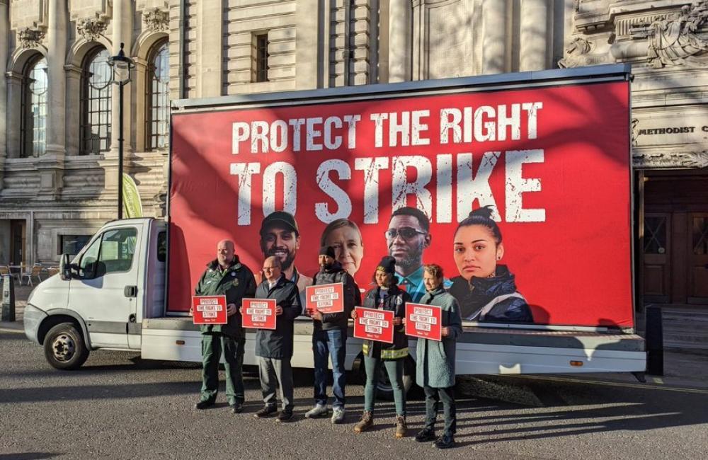 Five workers, including a firefighter, stand in front of a mobile billboard. The mobile billboard reads: protect the right to strike. The image is from the TUC day of action on February 1st 2023