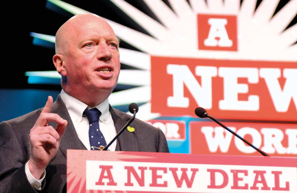 Matt Wrack speaking from podium in front of a new deal for working people sign