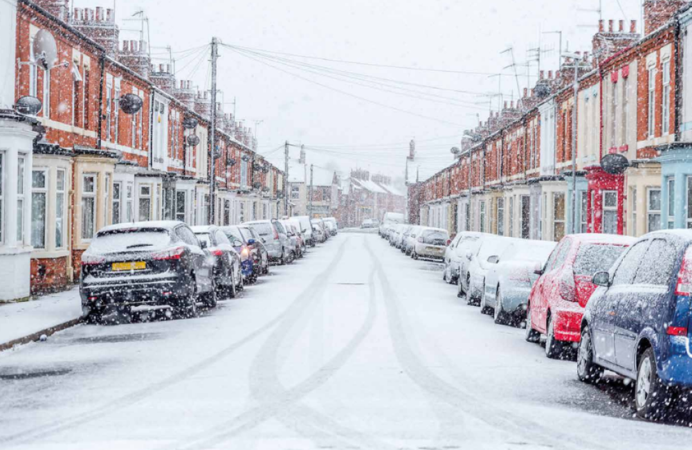 A snowy residential street with cars