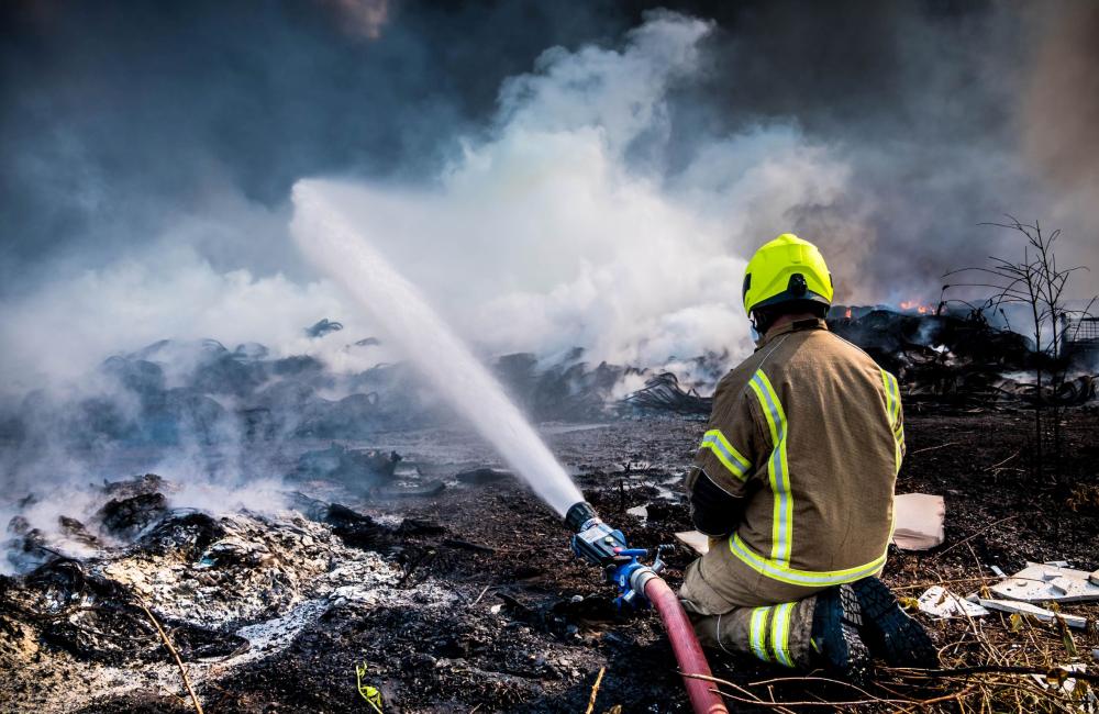 Firefighter sits next to hose while responding to a large fire outdoors
