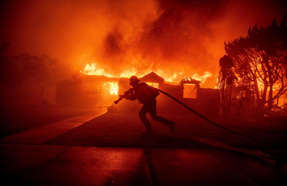 Firefighter drags a hose in front of burning buildings in LA
