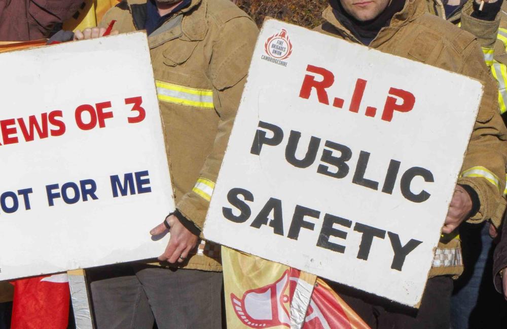 Two firefighters hold signs reading 'crews of three, not for me' and 'RIP public safety'