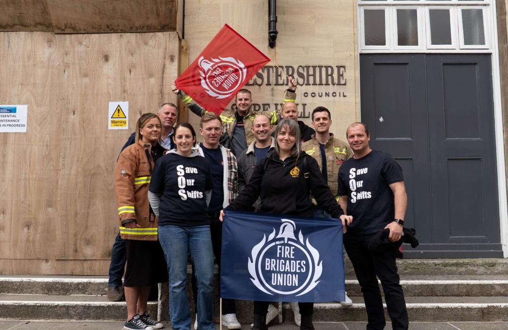A group of FBU members hold flags outside Gloucestershire county council building