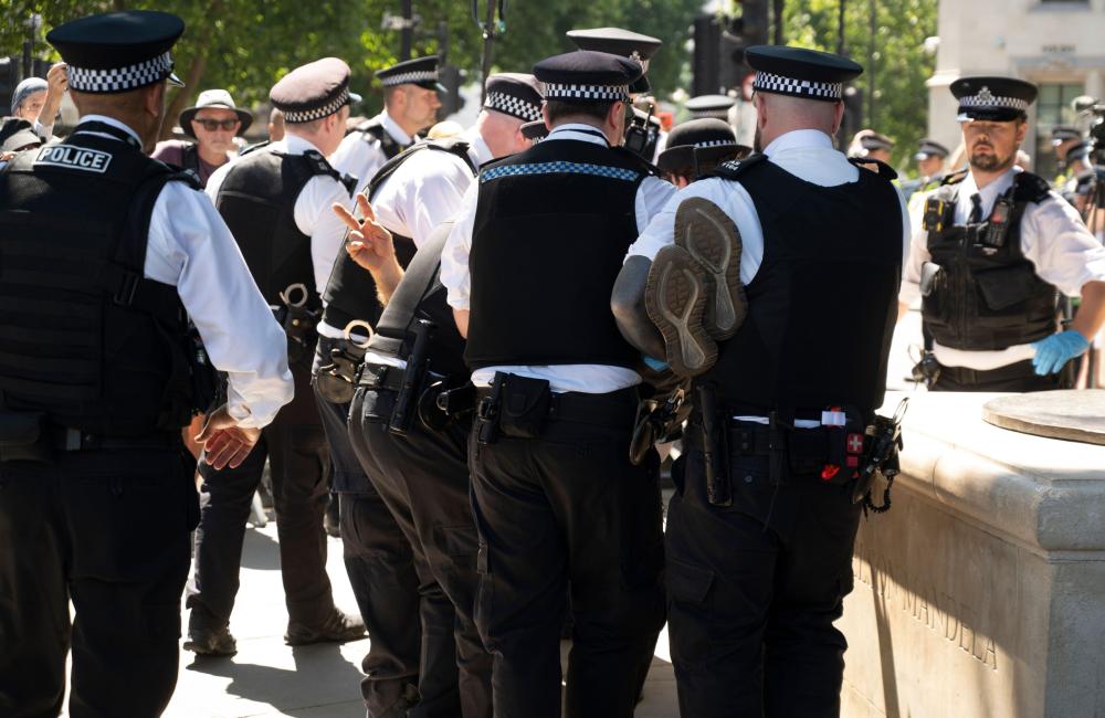 Police officers carry a protestor whose hand is visible making the peace sign