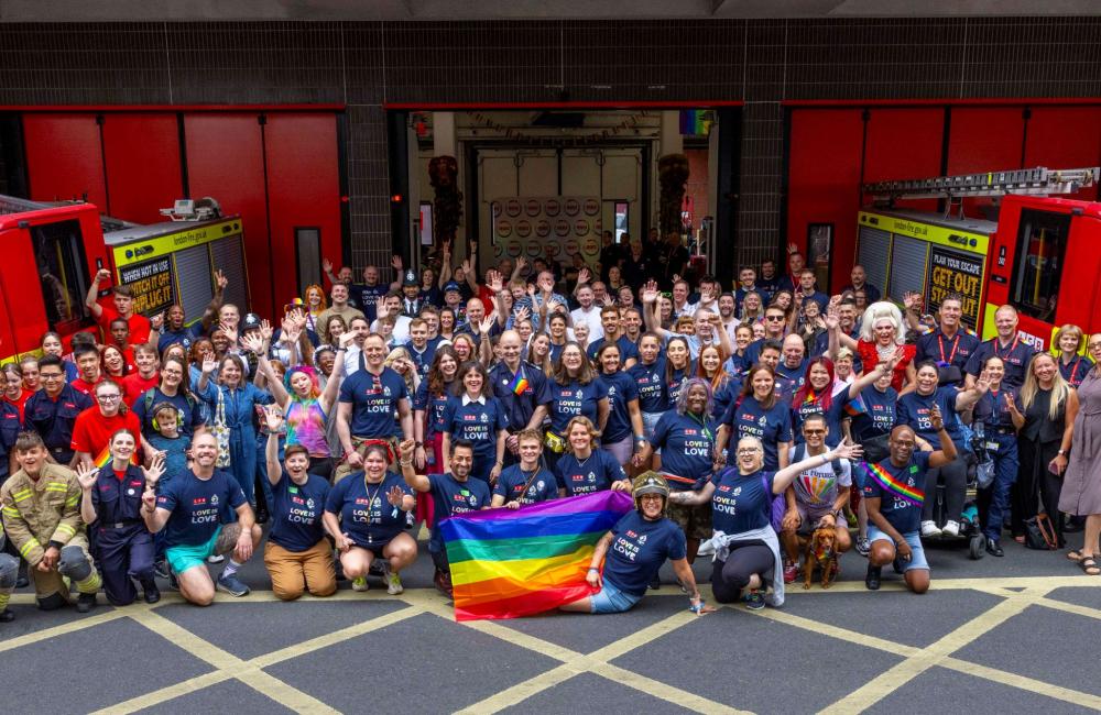 A large group photo with rainbow pride flags outside a fire station