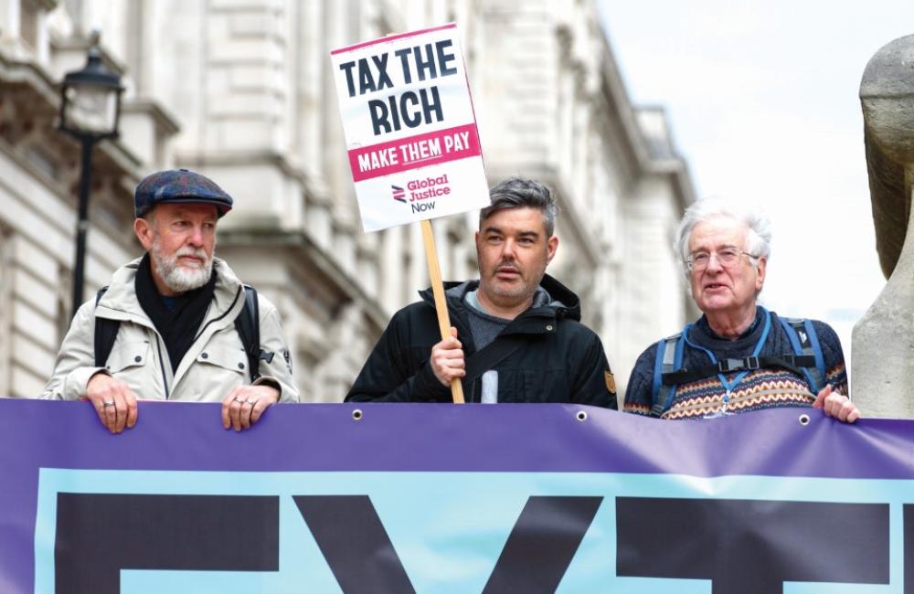 James O'Nions holding a placard reading "tax the rich"