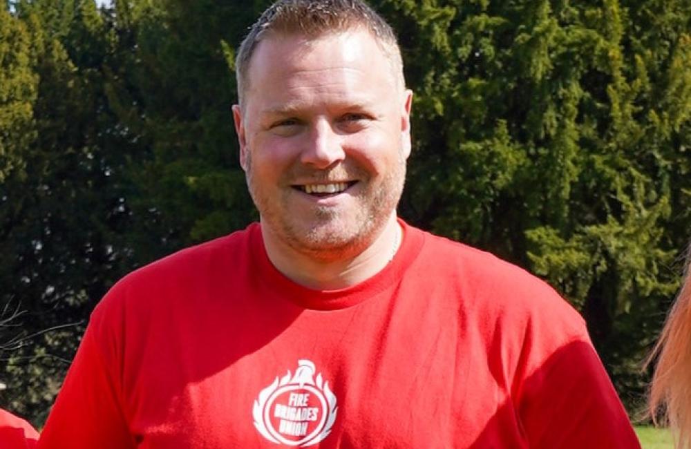 Ben Selby smiles at camera wearing a red "Equality matters" t shirt