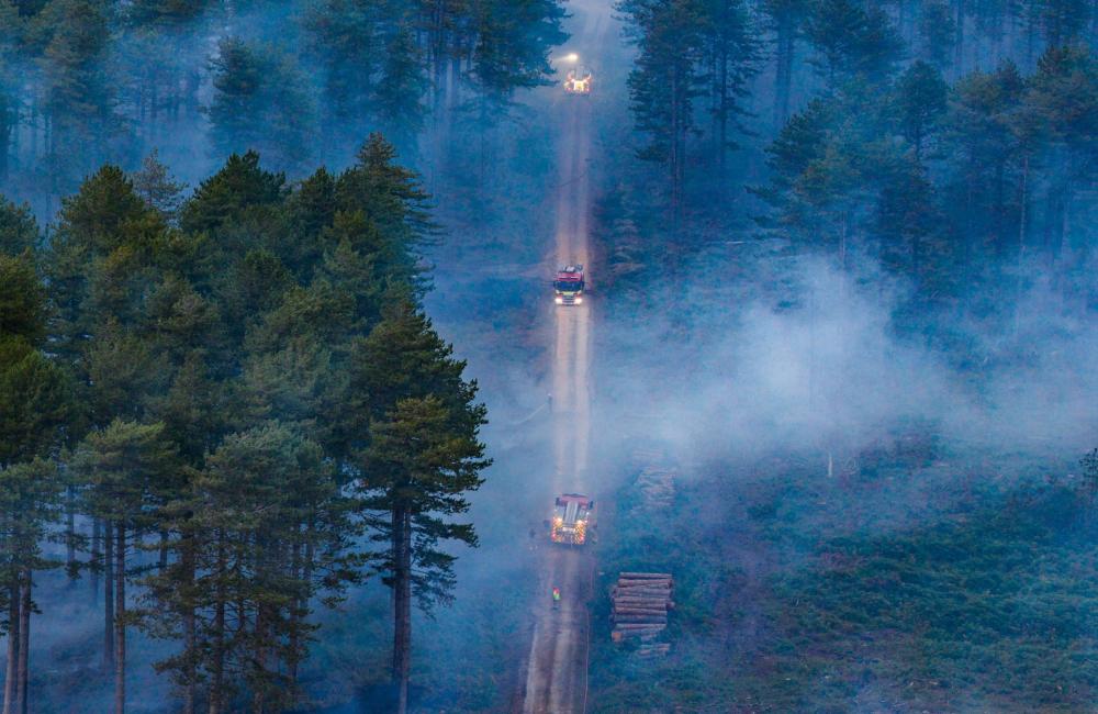Aerial view of two fire appliances driving on a long road through smoke of wildfire