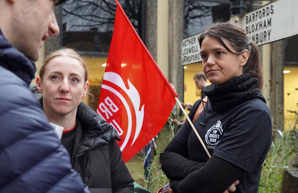 A woman holding an FBU flag while talking to fellow union members