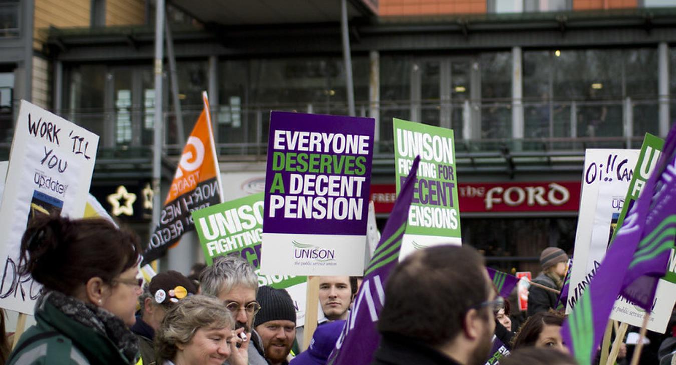 Crowd with people holding signs reading 'everyone deserves a decent pension'