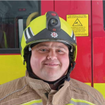 Dave Turner smiles at camera wearing firefighter helmet 