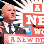 Matt Wrack speaking from podium in front of a new deal for working people sign