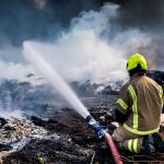 Firefighter sits next to hose while responding to a large fire outdoors