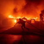 Firefighter drags a hose in front of burning buildings in LA