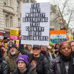 People at a protest against racism holding a placard reading 'the only minority destroying this country are the billionaires'