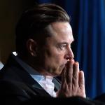 Elon Musk thinking and looking forwards with his hands up to his mouth