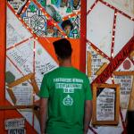 Firefighter wearing a t shirt reading 'FBU demands safe homes for all' looks at the Grenfell memorial wall