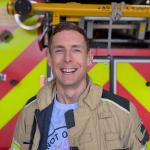 Tom Wass smiles at camera in front of a fire engine