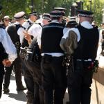 Police officers carry a protestor whose hand is visible making the peace sign