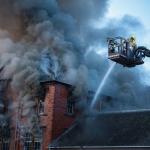 Firefighters on an aerial ladder platform over a burning roof