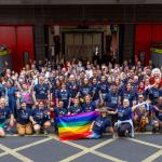 A large group photo with rainbow pride flags outside a fire station