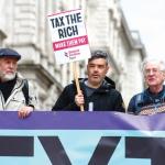 James O'Nions holding a placard reading "tax the rich"