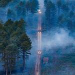 Aerial view of two fire appliances driving on a long road through smoke of wildfire