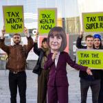 Protestors hold 'tax the rich signs', with one dressed as Rachel Reeves